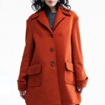 Žena nosi kratki, narandžasti oversize kaput.