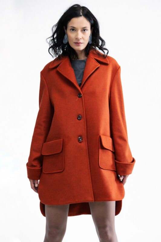 The woman wears a short, orange oversize coat.