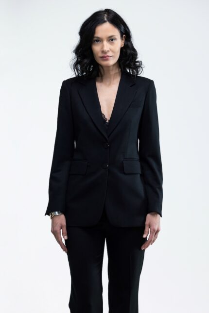 The woman wears a black waisted blazer and black skinny pants.