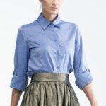 Žena nosi plavu LINA košulju od pamuka i zlatnu suknju.