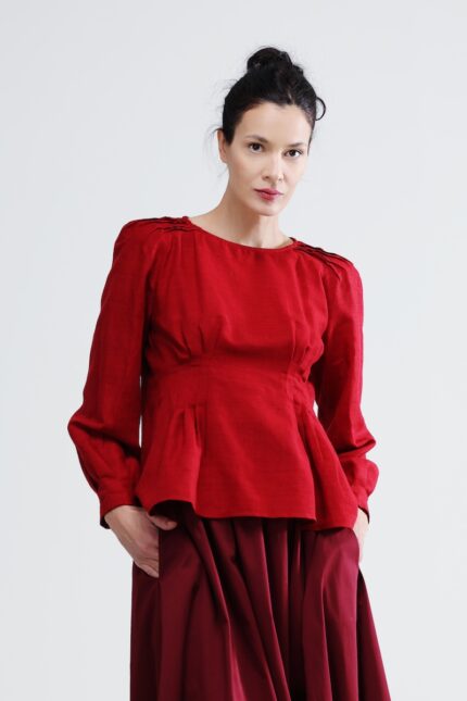 The woman wears a red blouse with long sleeves and a burgundy skirt.