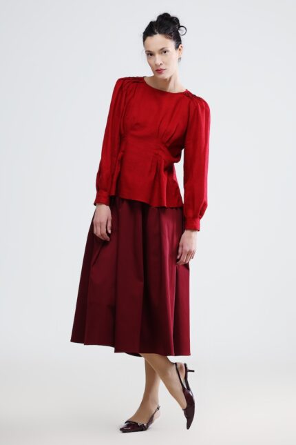 The woman wears a red blouse with long sleeves and a burgundy skirt.