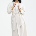 The girl wears a cream white tie coat.