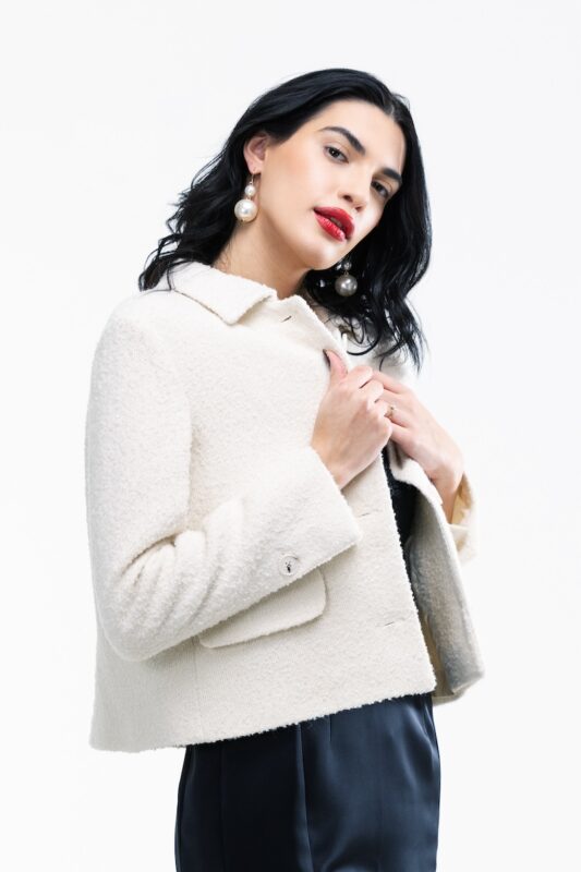 The girl wears a short white boucle blazer.