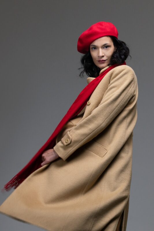 The woman wears a beige XENIA midi coat with a double-breasted button.