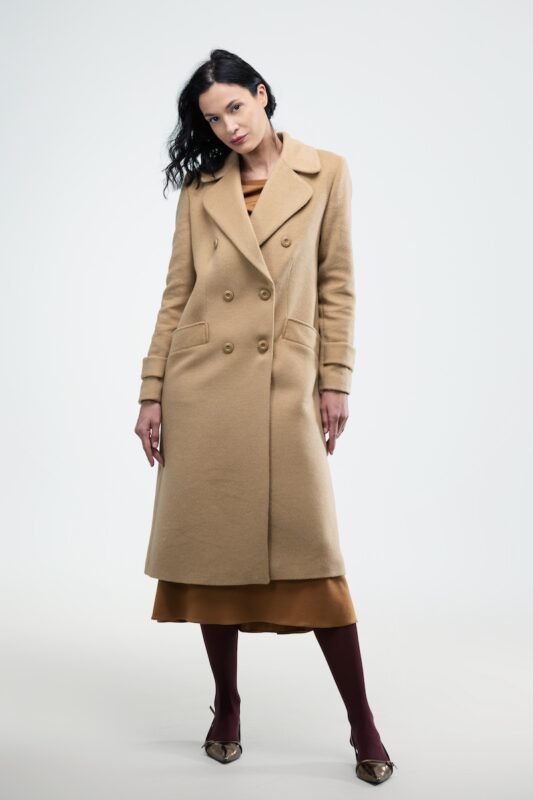 The woman wears a beige XENIA midi coat with a double-breasted button.