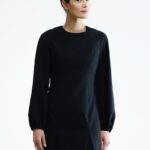 Žena nosi kratku crnu haljinu sa crnim rukavima.