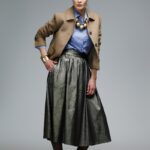 Žena nosi suknju od zlatnog štrasa i bež kratki blejzer.