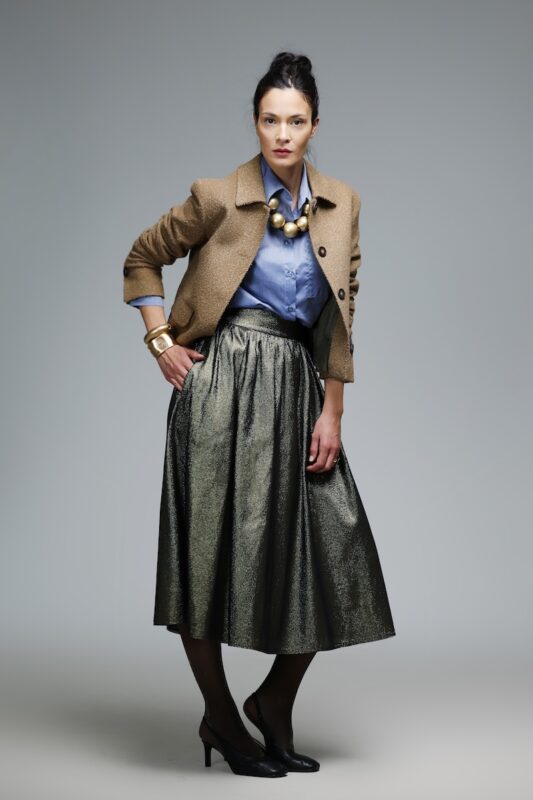 Žena nosi suknju od zlatnog štrasa i bež kratki blejzer.