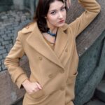 Devojka nosi bež kaput sa dvorednim kopčanjem.