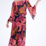 Manekenka nosi dugu dezeniranu haljinu sa lepršavim rukavima i spuštenim ramenima.