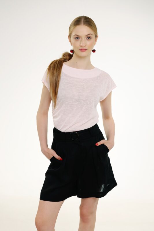Model nosi crni laneni šorts i roze majicu kratkih rukava.