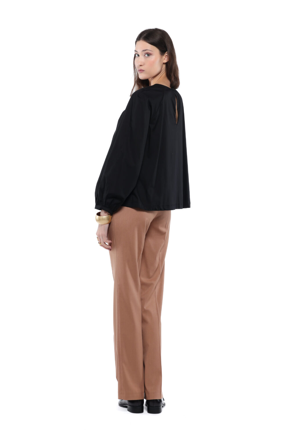 Model nosi crnu ALEKSA bluzu uparenu sa kamel pantalonama na beloj pozadini.