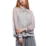 Devojka nosi svilenu bluzu sa tirkiznim tufnama sa dugim rukavima.