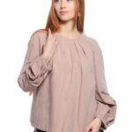 Devojka nosi bež pamučnu bluzu sa dugim rukavima.