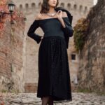 The model is wearing a black satin dress that flares at the bottom.