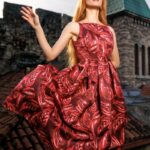 Devojka nosi midi crvenu dezeniranu haljinu na bretele.