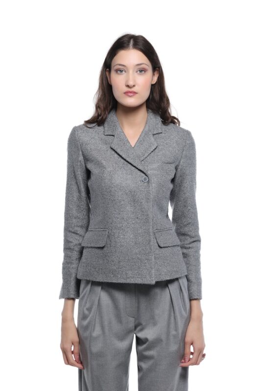 Model nosi sivi GIGI blejzer sa klasičnim reverima, jednim dugmetom i džepovima sa patnama. Blejzer je uparen sa sivim širokim pantalonama na beloj pozadini.
