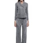 Model nosi sivi GIGI blejzer sa klasičnim reverima, jednim dugmetom i džepovima sa patnama. Blejzer je uparen sa sivim širokim pantalonama na beloj pozadini.