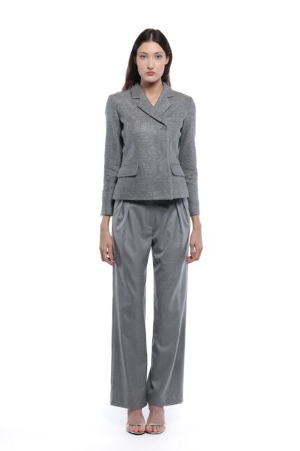 Model nosi sivi GIGI blejzer sa klasičnim reverima, jednim dugmetom i džepovima sa patnama. Blejzer je uparen sa sivim širokim pantalonama na beloj pozadini.