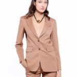 The model is wearing a tailored LETITIA blazer in a warm camel color, featuring wide classic lapels and double-breasted closure with two buttons. The blazer has flap pockets and a subtly shaped silhouette. It is paired with trousers in the same shade on a white background.