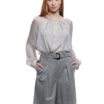 Devojka nosi duži sivi šorts sa pojasem oko struka iste boje u kombinaciji sa sivom svilenom bluzom.