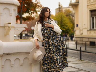 The model is wearing a midi patterned dress paired with a midi light beige coat.