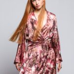 Devoja nosi dezeniranu prljavo roze haljinu mini dužine sa V izrazom.