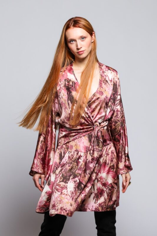 Devoja nosi dezeniranu prljavo roze haljinu mini dužine sa V izrazom.