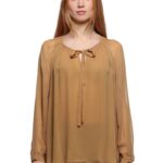 Devojka nosi svetlosmedju bluzu sa dugim rukavima u kombinaciji sa teget pantalonama.