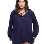 Devojka nosi svilenu teget košulju sa dugim rukavima u kombinaciji sa smedjim pantalonama.