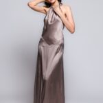 The model is wearing a maxi silk dress in a sand shade, tied around the neck.