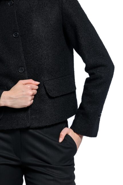 Devojka nosi crni blejzer sa kragnom i prednjim džepovima u kombinaciji sa crnim pantalonama.
