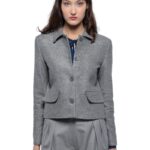 Devojka nosi sivi blejzer sa kragnom i prednjim džepovima u kombinaciji sa sivim pantalonama.