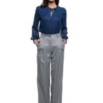 Devojka nosi sive pantalone u kombinaciji sa teget svilenom košuljom.