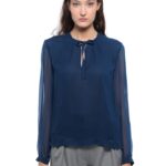 Devojka nosi teget bluzu sa dugim rukavima i svetlosivim pantalonama.