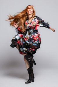 The model is wearing a black midi dress with a floral pattern and kimono sleeves.